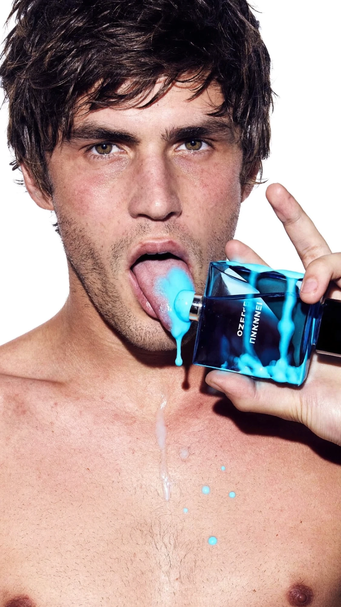 Fragrance concept: a model holds a blue perfume bottle dripping bright blue liquid onto his tongue, on white