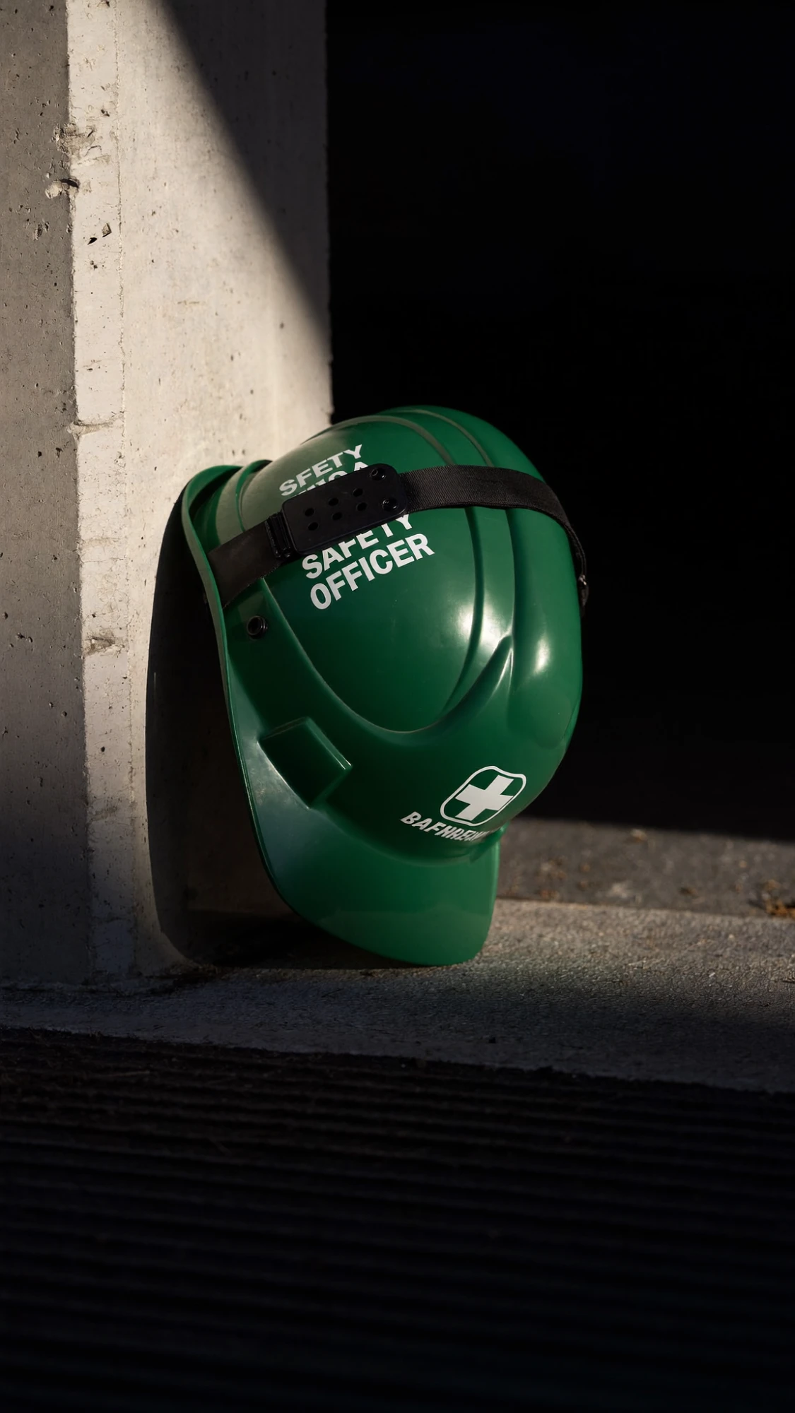 Green safety officer helmet resting against a sunlit concrete column
