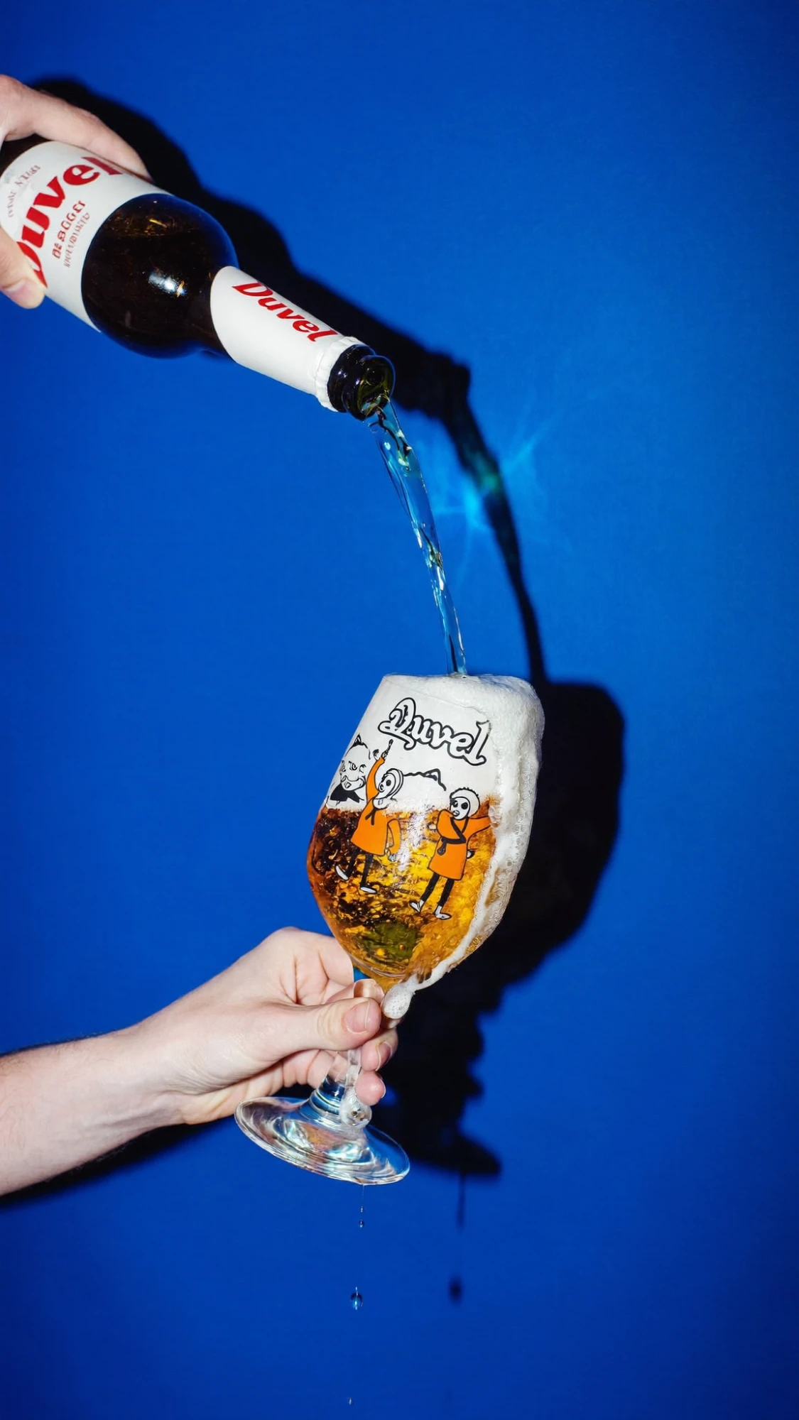 Concept for Duvel: beer poured from the bottle into a foaming illustrated glass on bright blue